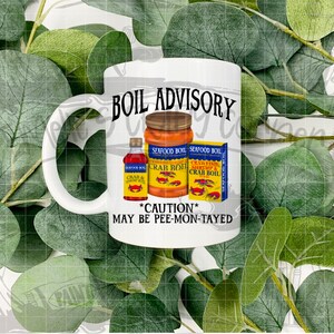 May include: White ceramic mug with a black and white graphic that says "BOIL ADVISORY" with a red crab and yellow and blue seafood boil cans. The text below the cans says "*CAUTION* MAY BE PEE-MON-TAYED"