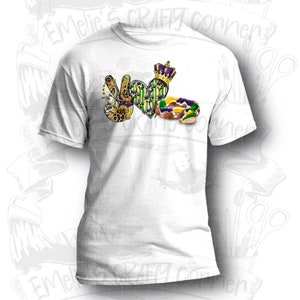 May include: White t-shirt with a purple, green, and gold peace sign, heart, and king cake design. The design includes the words "I Love Mardi Gras".