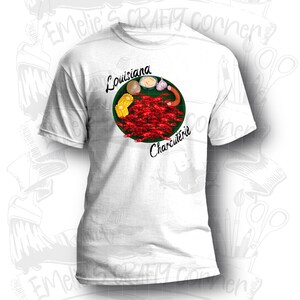 May include: White t-shirt with a green circle design featuring crawfish, corn on the cob, a potato, garlic, and a sausage. The text "Louisiana Charcuterie" is written around the circle.