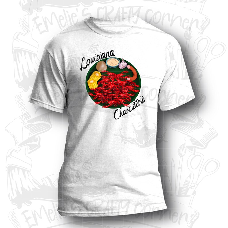May include: White t-shirt with a green circle design featuring crawfish, corn on the cob, a potato, garlic, and a sausage. The text "Louisiana Charcuterie" is written around the circle.