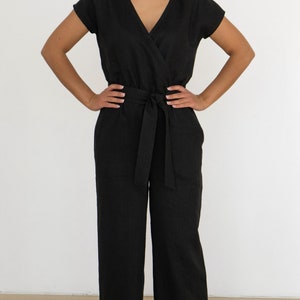 Woman wearing a black linen jumpsuit with short sleeves, V-neck wrap front, waist tie, and wide-leg pants – minimalist, elegant outfit suitable for casual or semi-formal occasions.