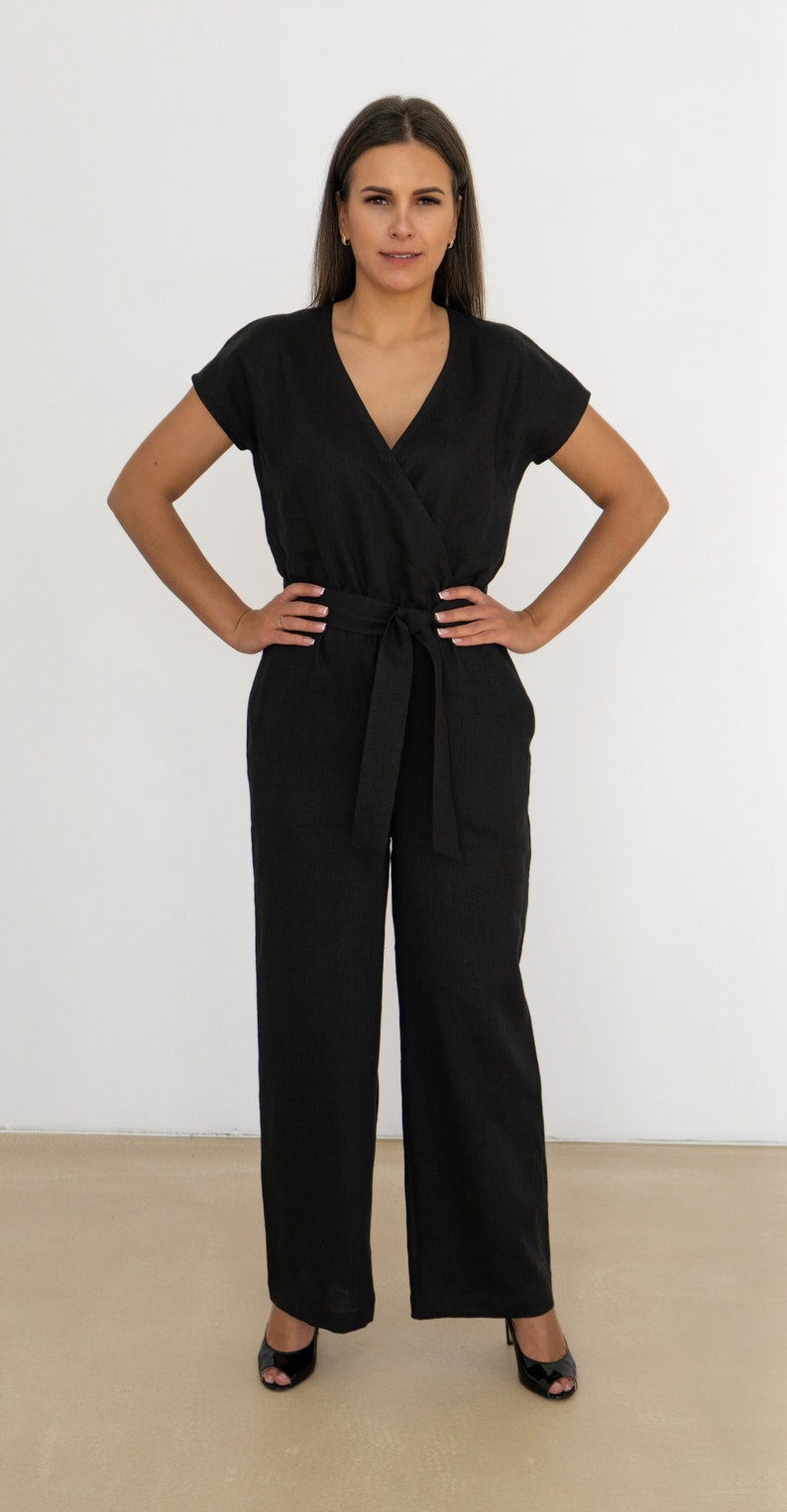 Woman wearing a black linen jumpsuit with short sleeves, V-neck wrap front, waist tie, and wide-leg pants – minimalist, elegant outfit suitable for casual or semi-formal occasions.