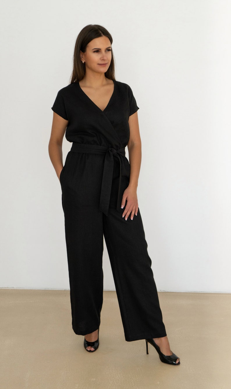 Woman wearing a black linen jumpsuit with short sleeves, V-neck wrap front, waist tie, and wide-leg pants – minimalist, elegant outfit suitable for casual or semi-formal occasions.
