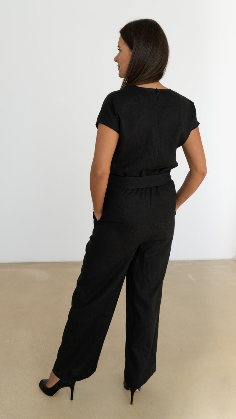 Back view of a woman wearing a black linen jumpsuit with short sleeves, tailored waistband, and wide-leg pants, styled with black heels – elegant and minimalist outfit for various occasions.