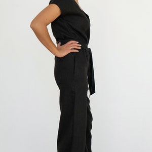 Woman wearing a black linen jumpsuit with short sleeves, V-neck wrap front, waist tie, and wide-leg pants – minimalist, elegant outfit suitable for casual or semi-formal occasions.