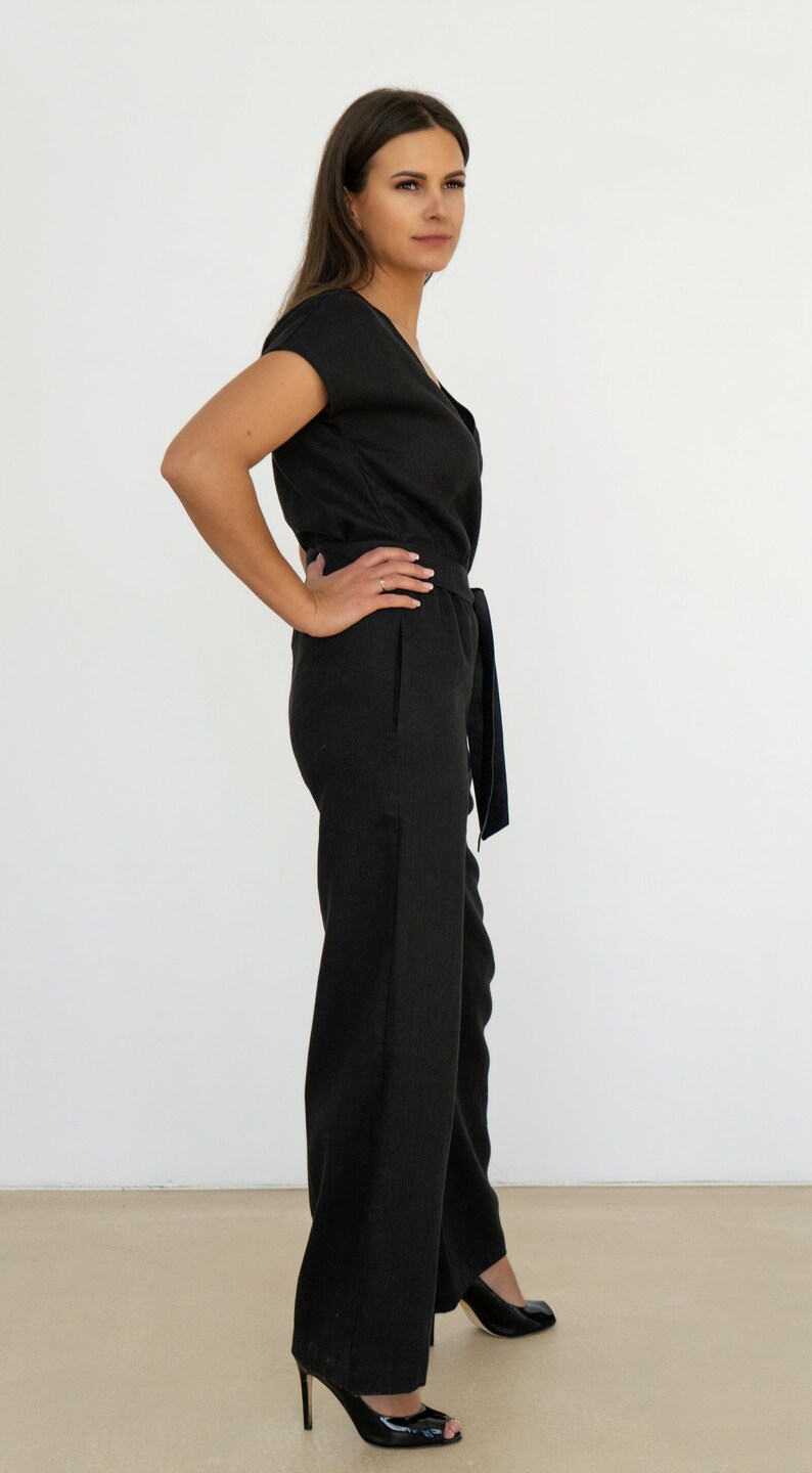 Woman wearing a black linen jumpsuit with short sleeves, V-neck wrap front, waist tie, and wide-leg pants – minimalist, elegant outfit suitable for casual or semi-formal occasions.