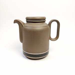 May include: A brown ceramic teapot with a lid and a black and white stripe around the middle.