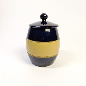 May include: A blue and tan ceramic jar with a lid. The jar has a rounded shape and a band of tan around the middle.