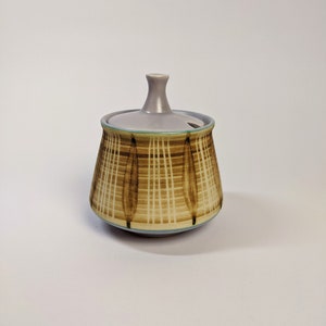 May include: A ceramic sugar bowl with a lid. The bowl is decorated with a brown and white striped pattern. The lid is a light purple colour.