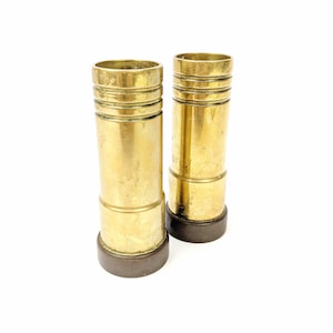May include: Two gold metal candle holders with a brown base. The candle holders are cylindrical and have a textured surface.