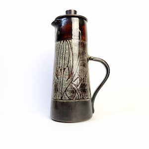 May include: A tall ceramic coffee pot with a dark brown lid and handle. The body has a decorative pattern in shades of grey and brown. The base is a darker shade of brown.