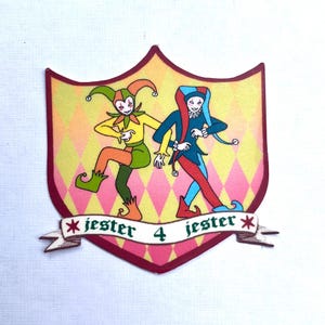 May include: A shield-shaped patch featuring two jesters in colorful costumes against a yellow and pink diamond pattern. One jester wears green and orange, the other blue and red. A white banner at the bottom displays the text jester 4 jester.