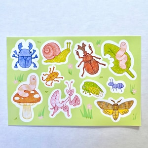 May include: A sticker sheet featuring colorful illustrations of various insects, including a blue beetle, a snail, a brown beetle, a worm on a leaf, a worm on a mushroom, a yellow bug, a pink praying mantis, a green cicada, a blue ant, and a yellow moth.