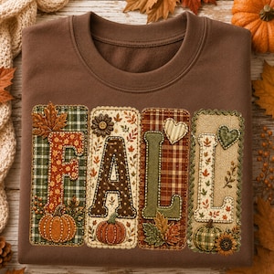 May include: A brown crewneck sweatshirt featuring four rectangular patches that spell out the word FALL. Each letter is decorated with autumn-themed fabric patterns, including plaid, gingham, pumpkins, leaves, and hearts in shades of orange, green, and brown.