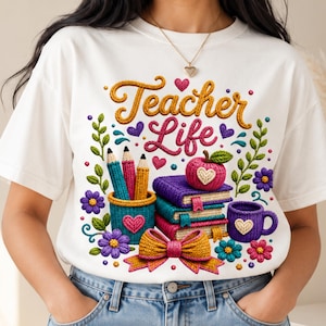 May include: A white t-shirt featuring a colorful graphic with the text Teacher Life in a yarn-like texture. The design includes a pencil holder with pencils, a stack of three books, a pink apple, a purple mug, and a bow, all with a knit appearance.