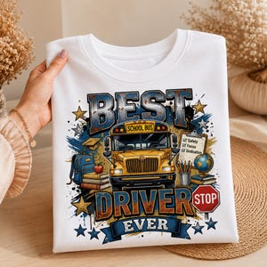 May include: A white t-shirt featuring a graphic of a yellow school bus with the text BEST DRIVER EVER. The design includes a blue backpack, books, an apple, a globe, a clipboard with the words Safety, Focus, Dedication, and a red stop sign.