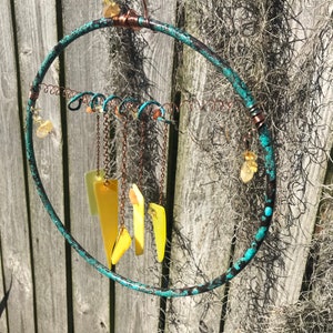 May include: A turquoise and copper-colored metal hoop with a hanging mobile of yellow glass pieces and copper chains. The mobile is suspended from a copper hook at the top of the hoop.