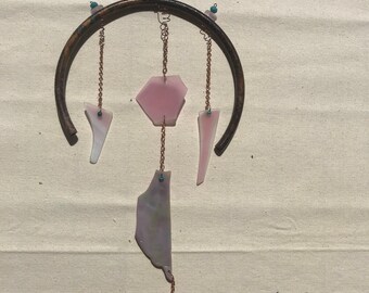 Könnte beinhalten: Ein rosa-brauner Glaswindspiel mit einer Glocke am Boden. Das Windspiel besteht aus verschiedenen Glasformen und hängt an einem Metallring.