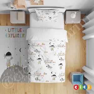 Puede incluir: Juego de cama blanco con un patrón repetido de un niño con un tocado de nativo americano, una cebra y las palabras "Little Explorers". El juego de cama incluye una funda de almohada, una funda nórdica y una alfombra con las palabras "Little Explorer" impresas.