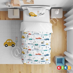 Könnte beinhalten: Ein Bettwäsche-Set mit weißem und blauem Muster und einem Design mit gelbem Auto und Ampel. Der Kissenbezug trägt den Namen "Emi".
