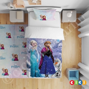 Könnte beinhalten: Ein weiß-blaues Bettwäsche-Set mit einer Szene von Elsa und Anna aus Disneys Frozen. Das Bettwäsche-Set beinhaltet einen Bettbezug, einen Kissenbezug und einen Teppich mit einem sich wiederholenden Muster der Frozen-Charaktere.