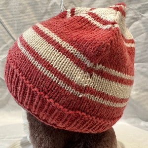 May include: A red and white striped knitted beanie hat. The hat is made of a soft, textured yarn and has a simple, classic design.