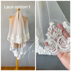May include: A white bridal veil with intricate lace detailing along the edges. The veil is displayed on a mannequin, showcasing the delicate floral and scrollwork patterns of the lace. The text "Lace option 1" is visible.