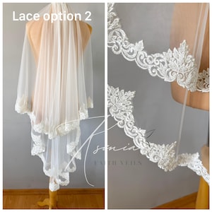May include: A sheer, ivory-colored bridal veil with delicate lace trim. The veil is displayed on a mannequin, showcasing the intricate floral and scrollwork patterns of the lace. The text "Lace option 2" is visible.
