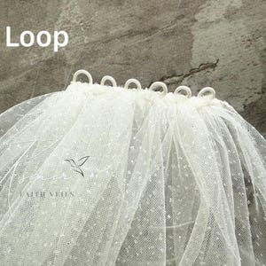 May include: A white bridal veil with a dotted pattern and loops at the top edge. The word "Loop" is written in white text at the top left. The veil has a delicate, airy appearance, suitable for weddings.