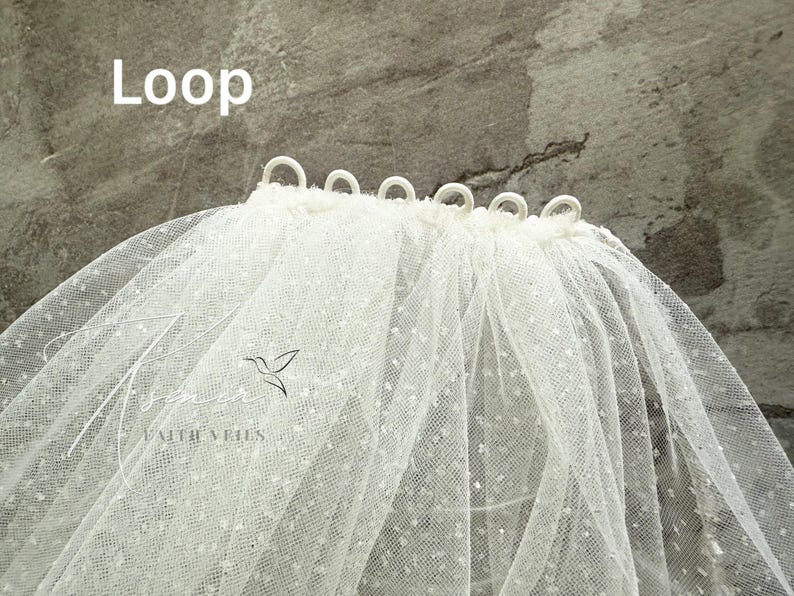May include: A white bridal veil with a dotted pattern and loops at the top edge. The word "Loop" is written in white text at the top left. The veil has a delicate, airy appearance, suitable for weddings.