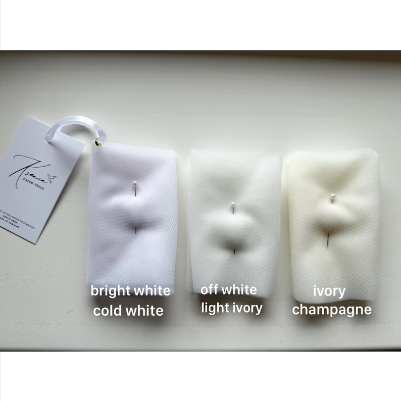 May include: Three samples of bridal veil fabric in varying shades of white: bright white/cold white, off white/light ivory, and ivory/champagne. Each sample is pinned and labeled with its color name. A tag with the brand name is visible.
