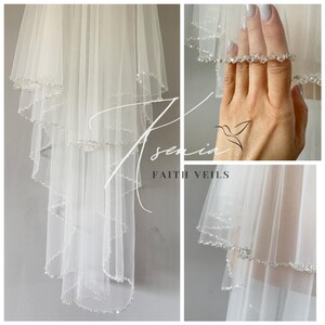May include: A white bridal veil with multiple layers, trimmed with sparkling crystals. The veil is sheer and delicate, with the text "Asenia Faith Veils" in the image.