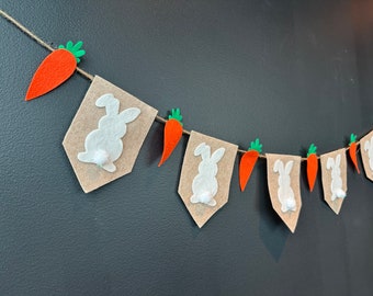 May include: A felt banner with alternating brown pennants and orange carrot shapes. Each pennant features a white bunny silhouette with a fluffy tail.