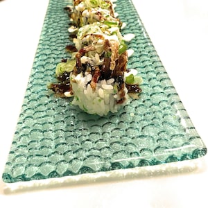 Può includere: Primo piano di un piatto di rotoli di sushi con condimenti fritti croccanti, cipolle verdi e salsa bianca. Il sushi è su un piatto verde testurizzato.