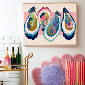 May include: A framed artwork featuring four colorful oyster shell paintings hangs above a pink sofa with a striped pillow and a fluffy purple pillow. A gold bar cart holds wine bottles and glasses. A white table displays a pineapple and lemons.