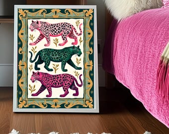 May include: A framed art print featuring three stylized leopards in pink, green, and magenta with black spots. The artwork has a decorative border with gold accents and is set against a cream background. The print is displayed on a wooden floor.