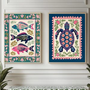 May include: Two framed art prints featuring colorful folk art designs. One print displays three fish in pink, blue, and black, surrounded by floral patterns. The other showcases a turtle with floral details. Both are framed in wood.