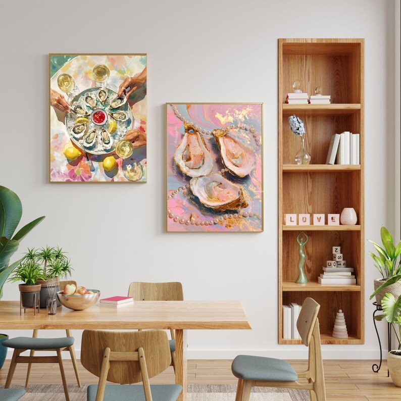 May include: Two framed art prints featuring oysters. One shows a platter of oysters with lemons and glasses of wine. The other features three oyster shells with pearl accents against a pink and gold background.