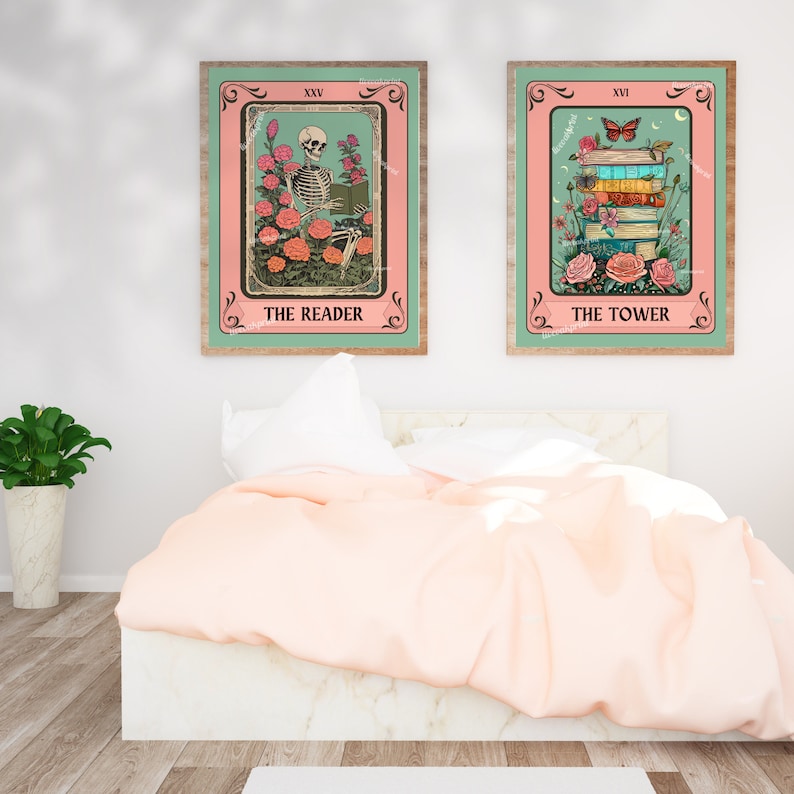 May include: Two framed tarot card prints. The Reader features a skeleton reading among roses, and The Tower shows a stack of books with a butterfly. Both have pink and teal backgrounds with wooden frames. The prints are displayed above a bed.