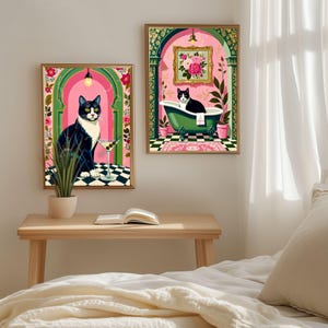 May include: Two framed art prints featuring black and white cats in whimsical settings. One print shows a cat with a martini, the other a cat in a green bathtub. Both have pink and green floral accents and gold frames.