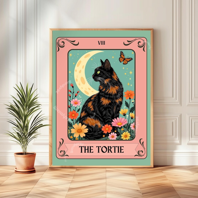 May include: A framed print featuring a black and orange tortoiseshell cat, a crescent moon, and a butterfly. The artwork is set against a teal background with colorful flowers and the text "THE TORTIE" at the bottom. The frame is a light green color.