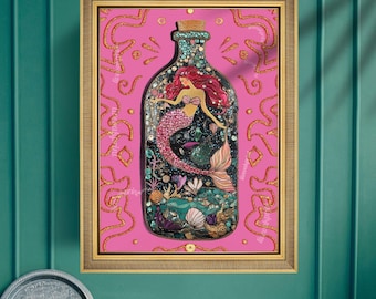 Op de afbeelding: Een ingelijst kunstwerk met een zeemeermin in een fles. De zeemeermin heeft rood haar en een roze staart, omringd door koraal en zeeleven. De achtergrond is roze met gouden details en de lijst is goudkleurig.