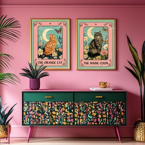 May include: Two framed cat tarot card art prints. One features an orange cat, the other a Maine Coon. Both have a floral and butterfly design with the text "The Orange Cat" and "The Maine Coon". The frames are gold.