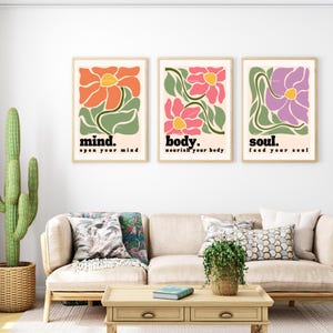 May include: Three framed art prints with floral designs in orange, pink, and purple. Each print features a flower with green leaves and the words "mind. open your mind", "body. nourish your body", and "soul. feed your soul".
