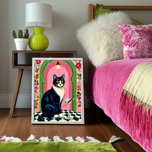 May include: A framed art print featuring a black and white cat with yellow eyes, sitting next to a martini glass. The artwork has a pink and green archway design with floral accents, set against a black and white checkered floor.