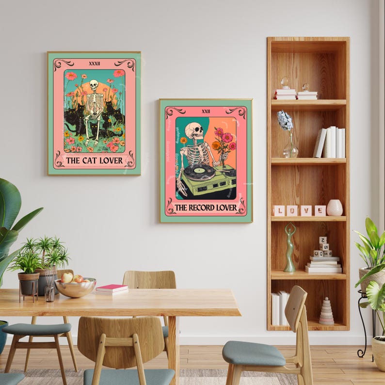 Op de afbeelding: Twee ingelijste kunstdrukken met een vintage tarotkaartontwerp. E&eacute;n toont een skelet met katten, de tekst "THE CAT LOVER". De andere toont een skelet met een platenspeler, met de tekst "THE RECORD LOVER". Beide hebben een roze en teal kleurenschema.