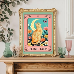 May include: A framed print featuring a buff tabby cat tarot card design. The artwork showcases a seated orange cat gazing at a butterfly, with a crescent moon and flowers in the background. The text reads "THE BUFF TABBY".