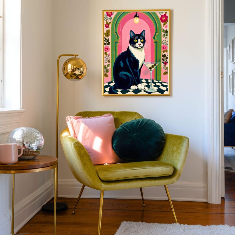 May include: A framed art print depicts a black and white cat with a martini glass. The cat sits on a checkered surface in front of a pink archway with floral accents. The print is in a gold frame.