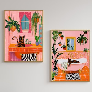 May include: Two framed art prints depicting colorful bathroom scenes. One shows a cat in an orange sink, the other a cat in a pink bathtub. Both feature pink walls, plants, and zebra-print accents.
