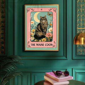 May include: A framed print featuring a Maine Coon cat illustration. The artwork has a pink border with floral and moon elements. The cat is brown and black, with the text "THE MAINE COON" at the bottom.